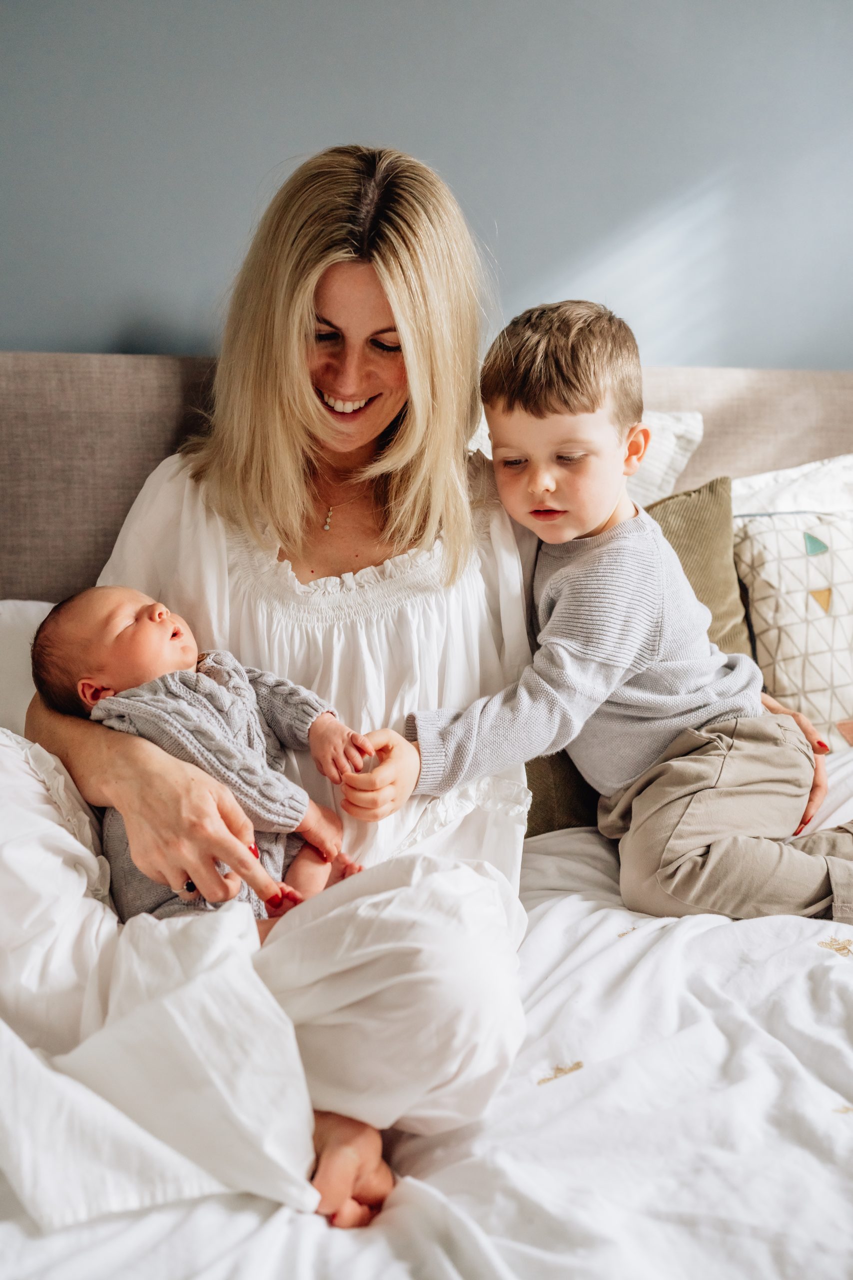 A mother and son sit on their bed next to each other, gazing down at the newborn baby in the mother's arms, during a photoshoot in Cheshunt